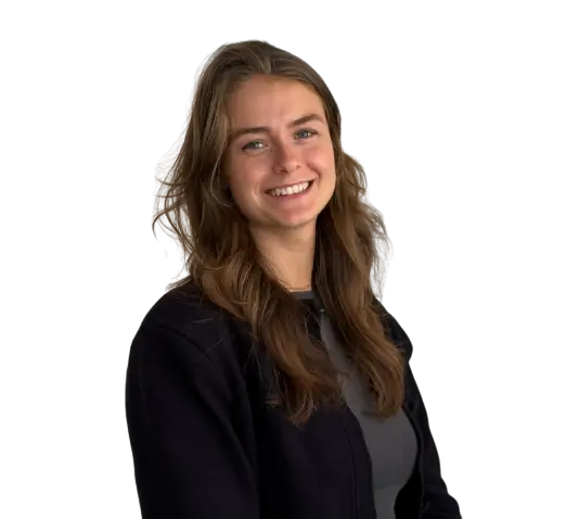 Vrouw met lang bruin haar in donker jasje en grijs shirt, lachend tegen een lichte achtergrond.