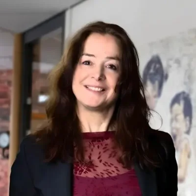 Portret van lachende vrouw met halflang bruin haar in kantooromgeving.