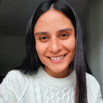 Vrouw met lang donker haar in witte trui, lachend en binnen gefotografeerd.