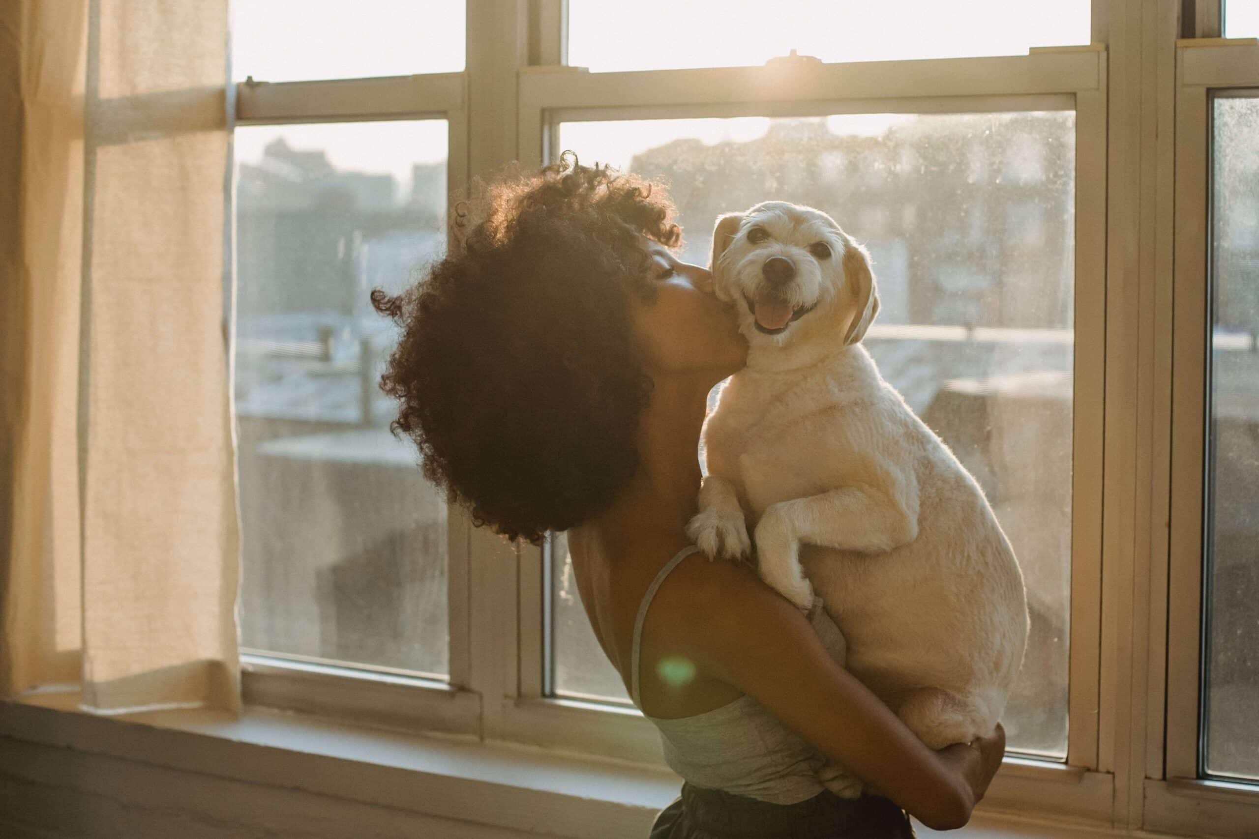 Een vrouw die thuis is en met haar hond knuffelt. Een mooi voorbeeld van JOMO.
