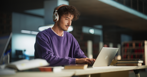 Man zit met koptelefoon op achter een laptop.