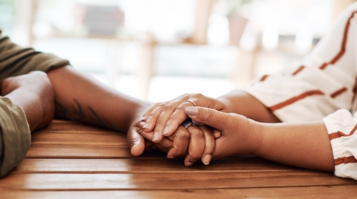 Een koppel dat liefdevol elkaars handen vasthoudt, als symbool voor verbinding en het samen werken aan het voorkomen van relatieproblemen.