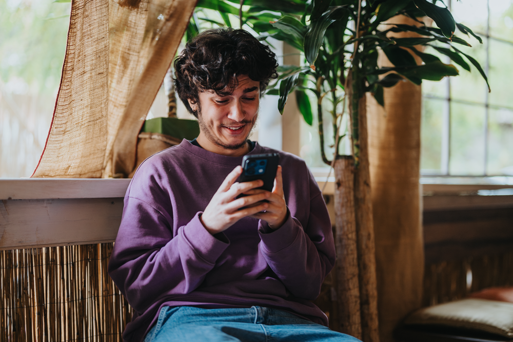 Vrolijke jongeman heeft zijn telefoon in z'n handen en kijkt ernaar.